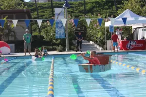 Kids racing cardboard boats across a pool.