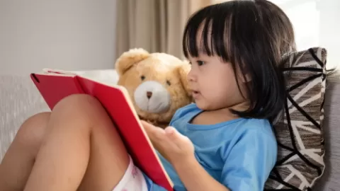 Young girl reading book with teddy bear