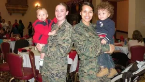 Two female Marines holding their toddler children at a holiday party