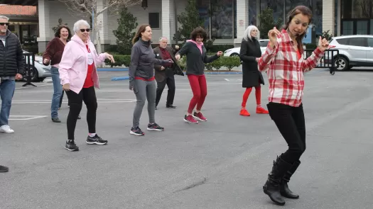 Group of people line dancing in a parking lot.