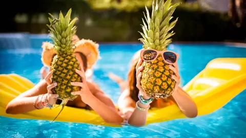 people on floatie in pool holding pineapples