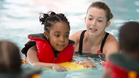 child swimming in pool with teacher