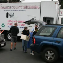 people with boxes of paper to shred loading a car