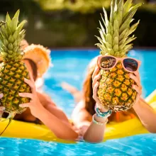 people on floatie in pool holding pineapples