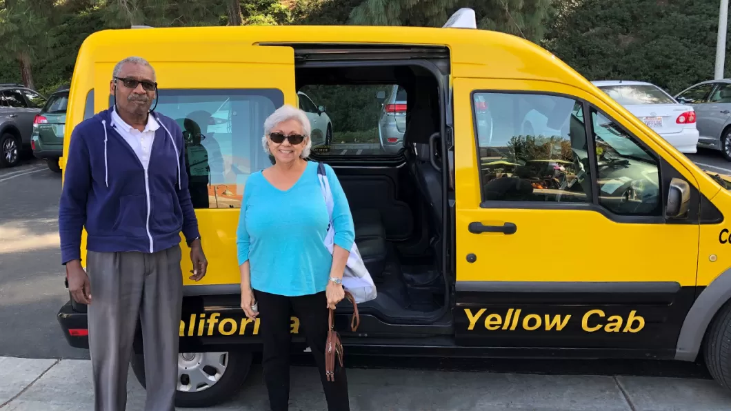 Senior woman and man standing outside of a California Yellow Cab.